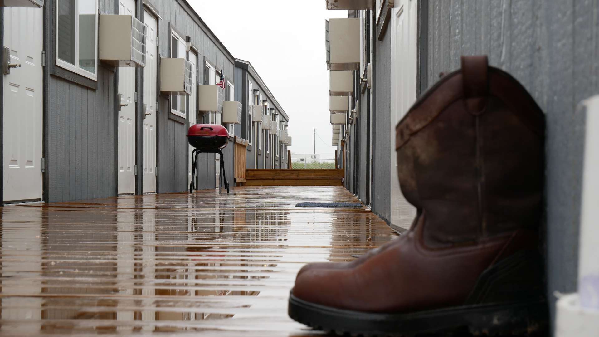 At one of Aries modular workforce camps, a light rain soaks into a wooden plank deck with rows of modular units serving as housing on either side.