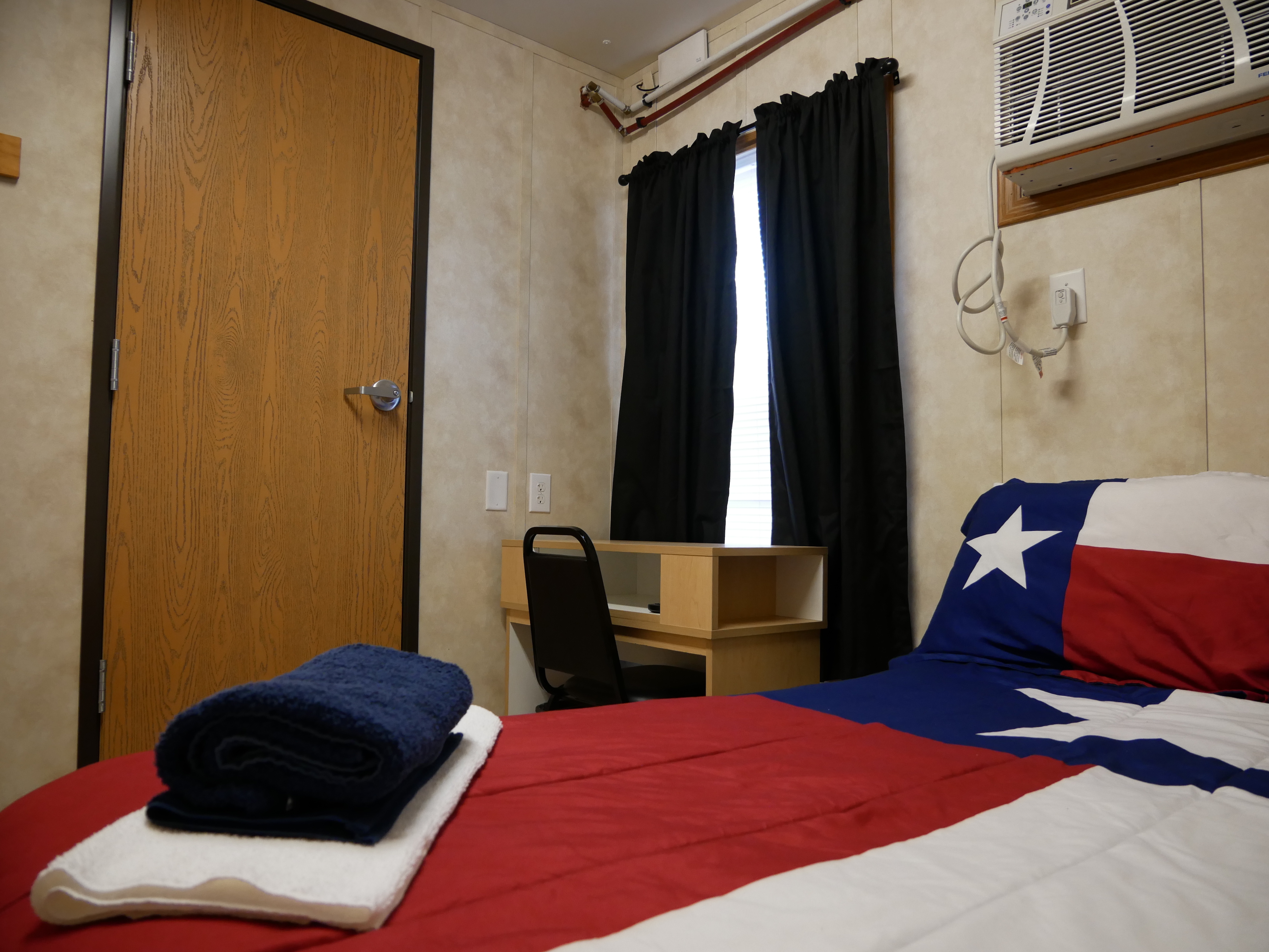 A picture of an interior of a room at a workforce housing camp, with Texas print bed sheets and blue curtains on the wall.
