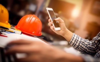 In a construction site, an arm holds a smartphone, suggesting that that the user is browsing the web from their mobile device.