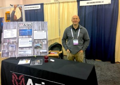 Aries Midwest Territory Manager Jason Ellis standing proudly at the Wisconsin State Education Convention behind the table at the Aries trade show booth surrounded by Aries brochures & branding.