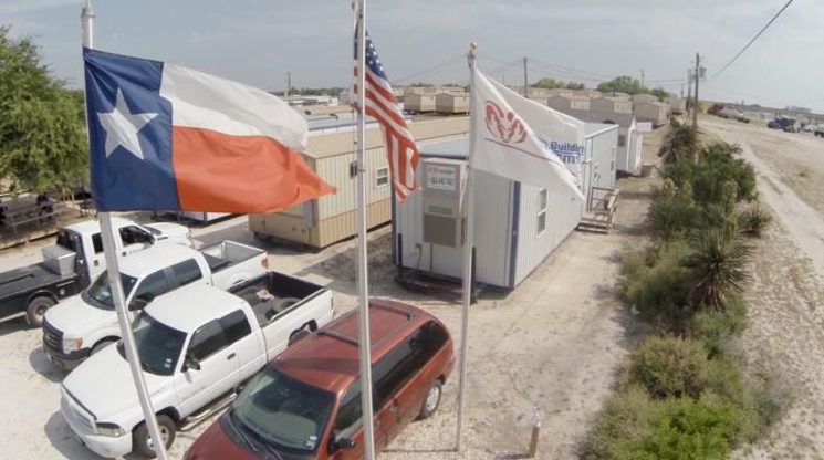 A hovering view of a workforce housing camp from Aries, with a Texas, American, and Aries flag flowing in the breeze.