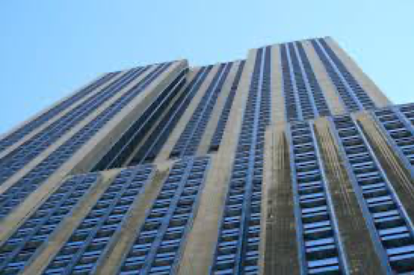 a ground-up, vertical view of a wide skyscraper with alternating blues window and grey columns that reaches high into a clear, light blue sky.