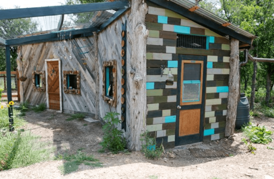 A wooden garden shed with orange doors and colorful tiles of green and turquoise, against patches of green grass and trees, on the grounds of Community First! Village.