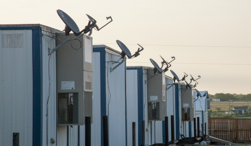 A row of Aries workforce housing units, white with blue panels, with satellite dishes and mechanical air handlers attached to the ends.