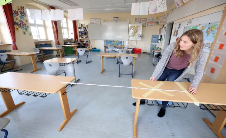 A teacher prepares her classroom by measuring to make sure there is enough space between the desks in order to comply with social distance guidelines. 
