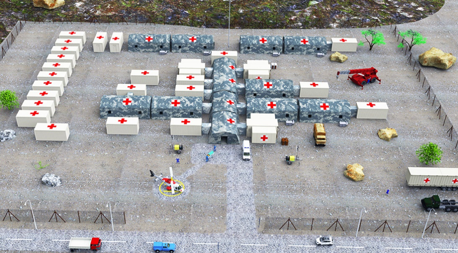 A slanted birds eye view of a compound of rectangular, trailer, portable buildings with red crosses on the top, and a few cars parked, and a fence around the compound. 
