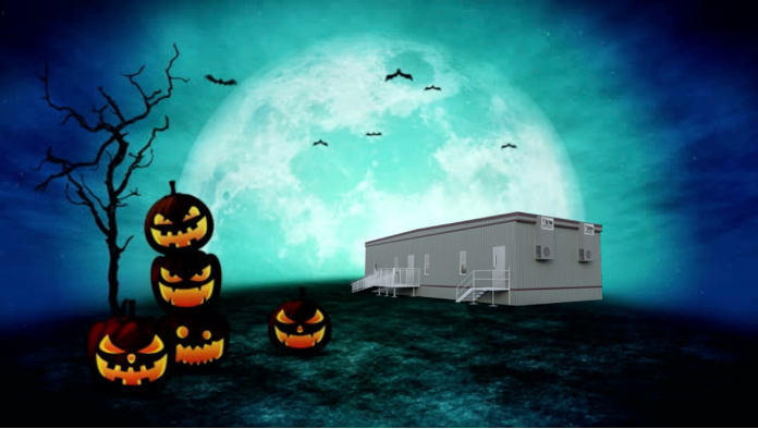 A creepy, animated-style Halloween scene on a dark night with a giant full moon in the background and a cluster of jack-o-lanterns in the foreground next to a leafless tree, and an Aries modular building atop a hill with bats flying overhead