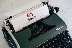Old fashioned typewriter holding a bright white sheet of paper with an maroon Aries’ ram letterhead with the word “NEWS.”