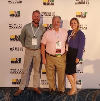 Aries’ very own Danny Heisler, Mike Roman, and Katie Roman-Leonard smile and pose in front of a Modular Building Institute backdrop at The World of Modular tradeshow, 2020.