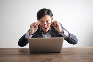 An attention-grabbing image of a man viewing something on his computer screen that we can’t see, as his facial expressions exclaim, “WOW!” and he holds his red-rimmed glasses a few inches from his face as if to say, “I need to see this closer!”