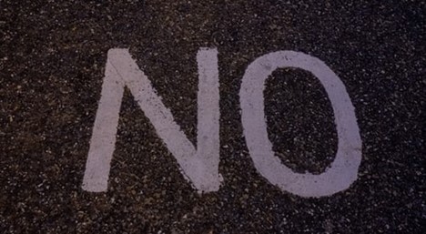 A large “no” sign in neat lavender letters painted on what looks to be an asphalt surface.