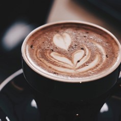 A close-up of café latte in a black coffee mug with a plant designed swirl in the foam.