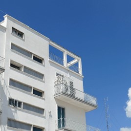 Corner view of the balconies on a tall, modern, white modular building in Alberobello, Puglia, Italy, a blue sky with a few clouds is in the background.