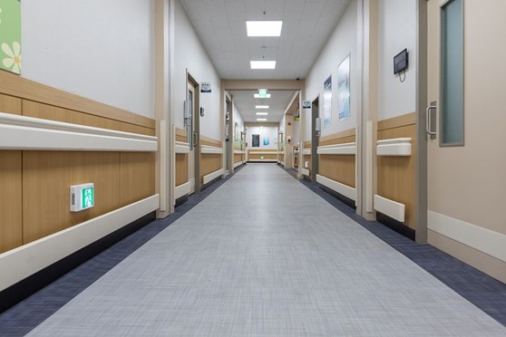 A picture of the length of a clean, well-lit hallway in a hospital with many closed doors on either side.
