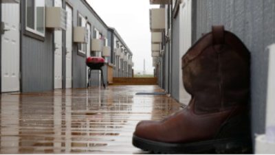 Photograph of a wet walkway between two rows of relief buildings with a pair of boots outside next to a door.