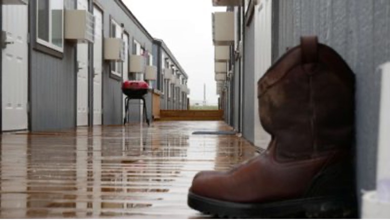 Photograph of a wet walkway between two rows of relief buildings with a pair of boots outside next to a door.