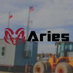 A blurred photograph of construction machinery pulling a beautiful modular building made by Aries. On the center of the image is the red ram logo of Aries.