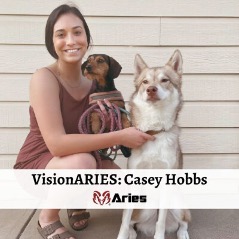 VisionAries, Casey Hobbs, smiling while holding her two cute dogs. At the bottom is a white banner that reads, “VisionAries: Casey Hobbs” and the red ram logo of Aries directly under it.