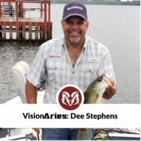 VisionAries, Dee Stephens, smiling while holding a caught fish by its mouth. At the bottom is a white banner that reads, “VisionAries: Dee Stephens” and an encircled Aries’ red ram logo directly above it.