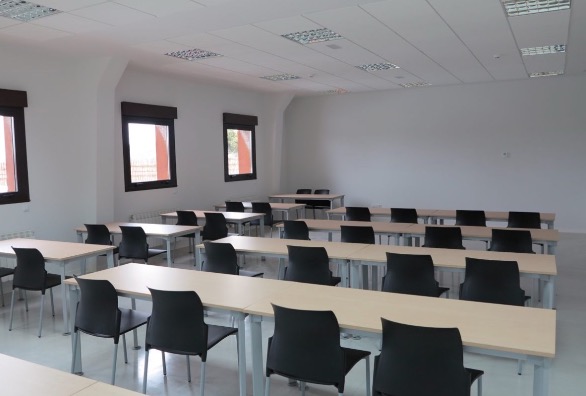 Interior of a pristine, empty classroom with rows of tables and neatly tucked chairs.