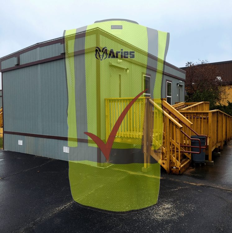 Aries portable building with a wooden ramp and walkway on a concrete lot. A faded image of a construction vest with the Aries logo and maroon checkmark overlays the photo.