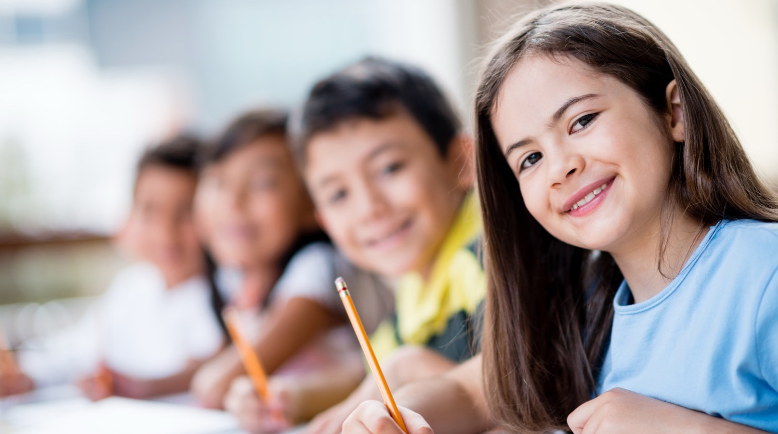 Kids smiling holding pencils in a classroom.