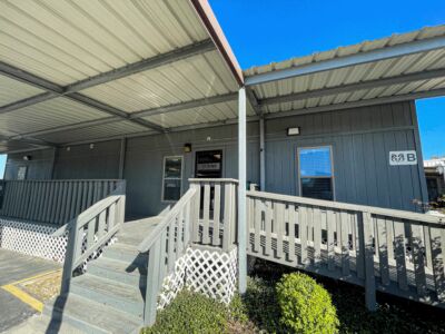 An exterior front view of Aries' Pasadena Office- Building B. It has wooden decking with a metal awning shading the front door.