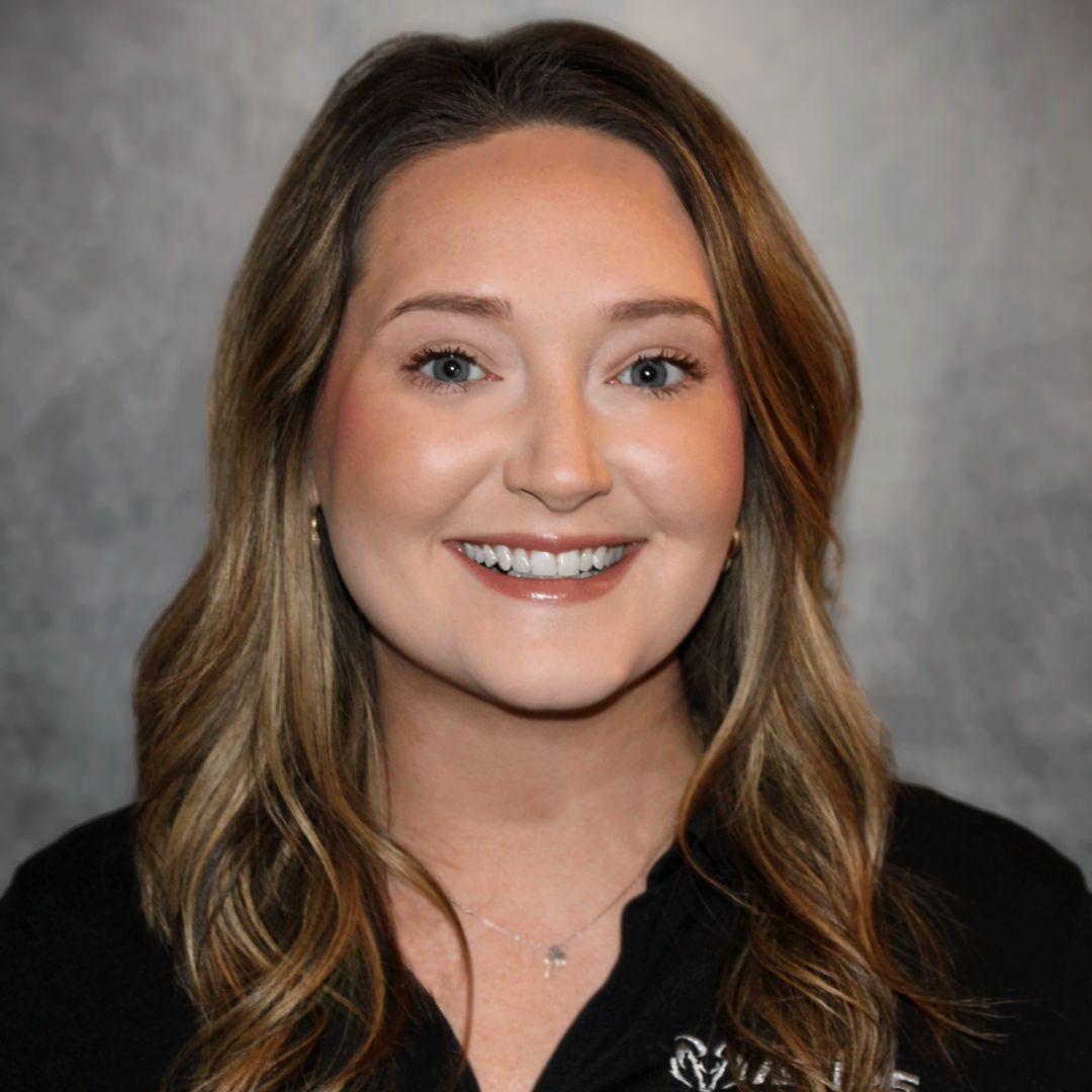 Headshot of Bailey Beck, Inside Sales Associate for Aries Buildings. She is smiling with brown wavy hair and is wearing a black collared shirt with the Aries logo on it.