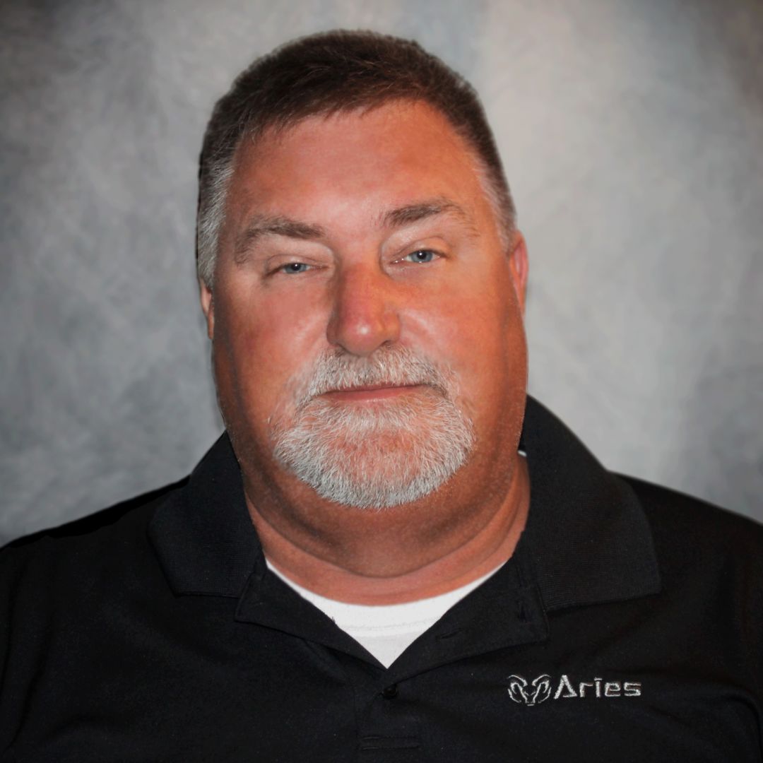 Headshot of Billy Beck, Territory Sales Manager for Aries Buildings. He has a mustache and beard and is wearing a black collared shirt with the Aries logo on it.