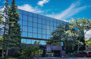 Photo of Aries Buildings' office in Bellevue, WA. It is a large building covered in glass windows surrounded by tall trees.