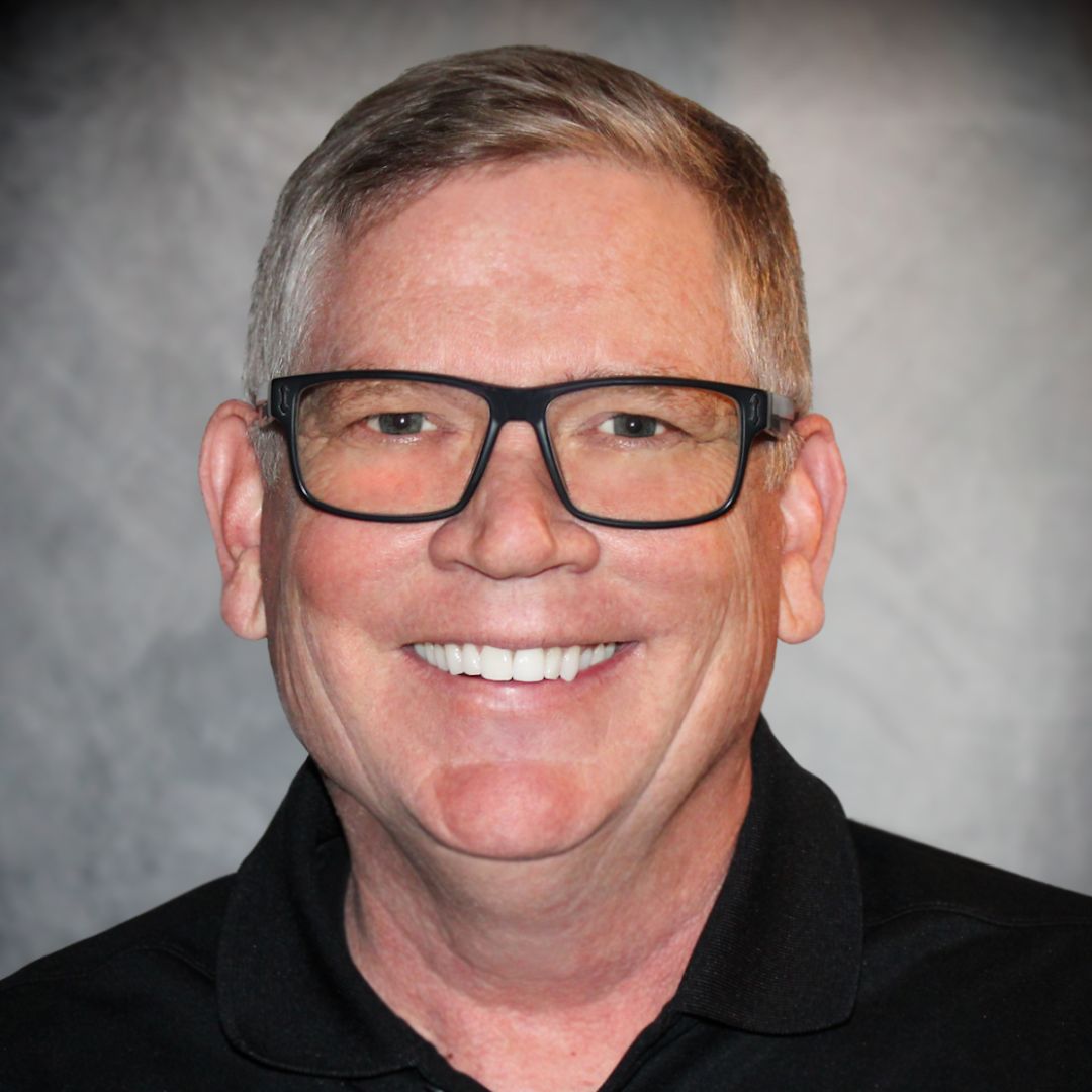 Headshot of Dan McGinnis, Aries' Regional Sales Manager in Centennial, CO. He is wearing a black collared shirt and black-rimmed glasses.