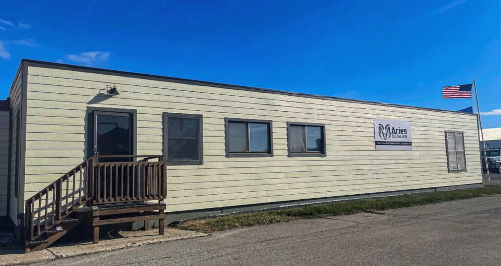 Photo of Aries' Rochester office, a mobile office trailer with an Aries sign and a wooden ramp leading to the front door.