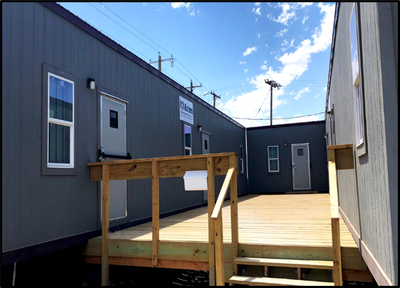 Mobile office with wooden stairs and decking, with a blue sky on a sunny day.