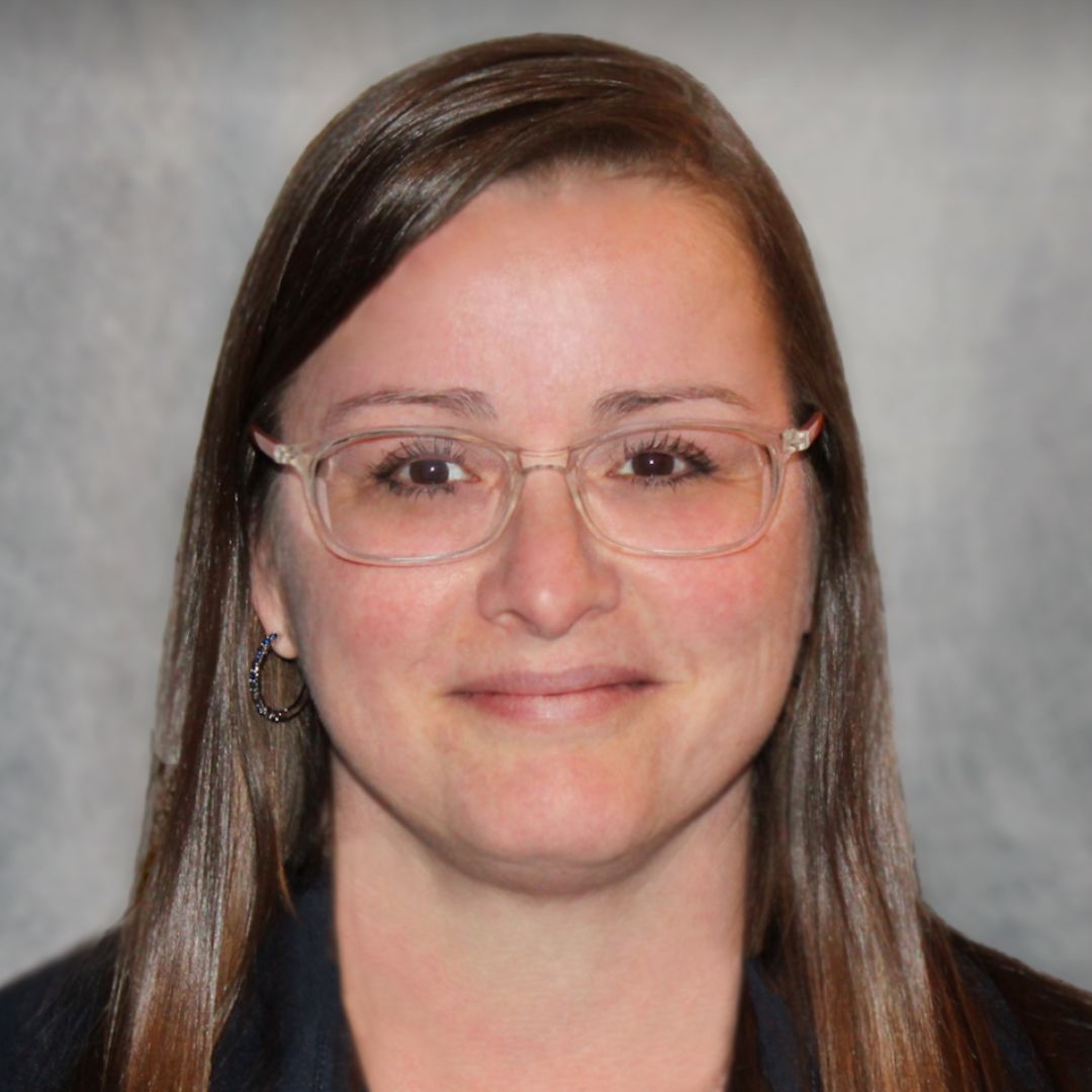 Headshot of Christina McAllister, Sales Associate for Aries Buildings in Clayton, NC. She has long brown hair, glasses, and is wearing a black collared shirt.