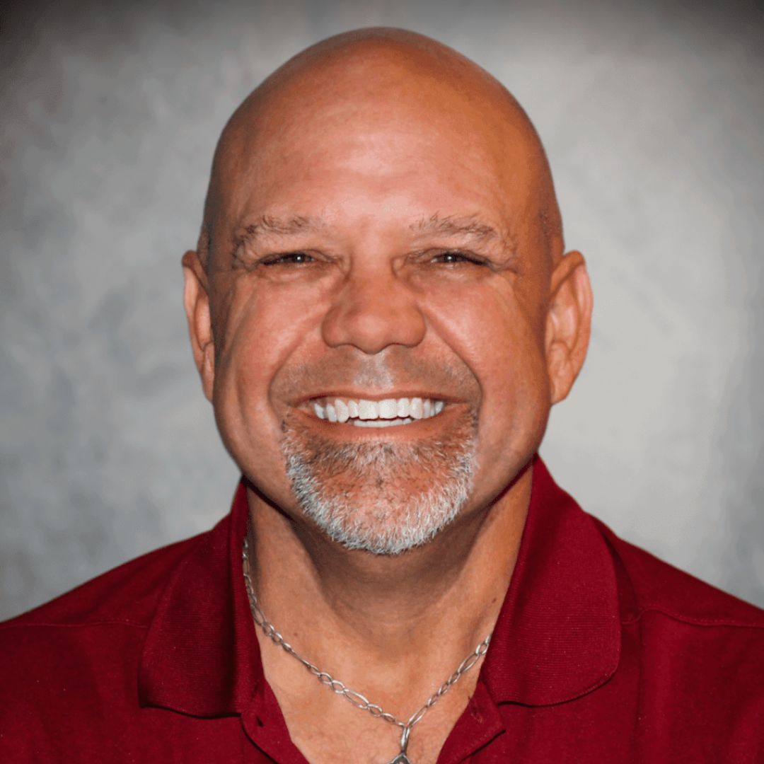 Headshot of Dee Stephens, Sales Associate for Aries Buildings in Seguin, TX. He is bald, has a beard, and is wearing a maroon collared shirt.