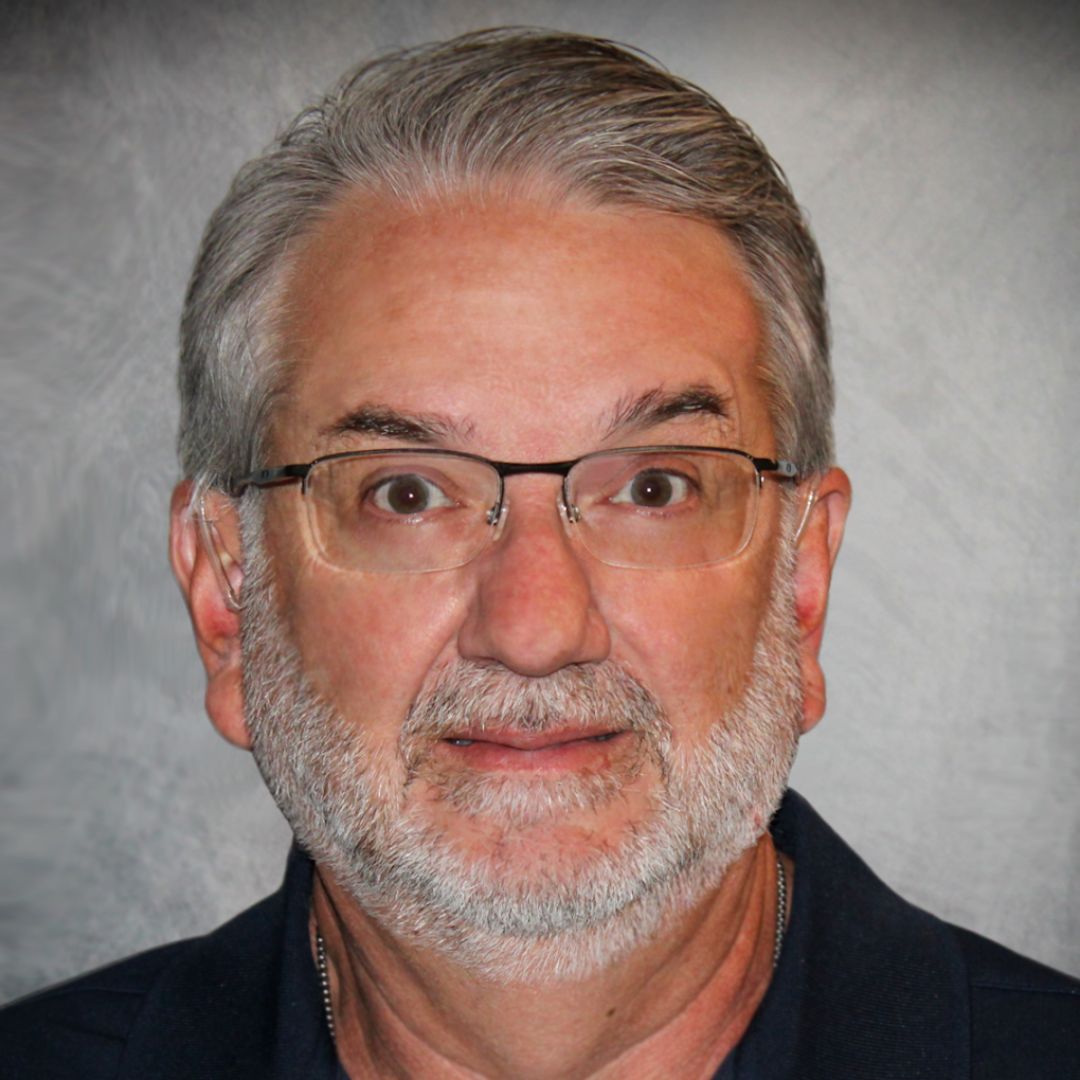 Headshot of Ken Kalsch, Territory Sales Manager for Aries Buildings in Clayton, NC. He has gray short hair and facial hair, is wearing glasses, and a black collared shirt.