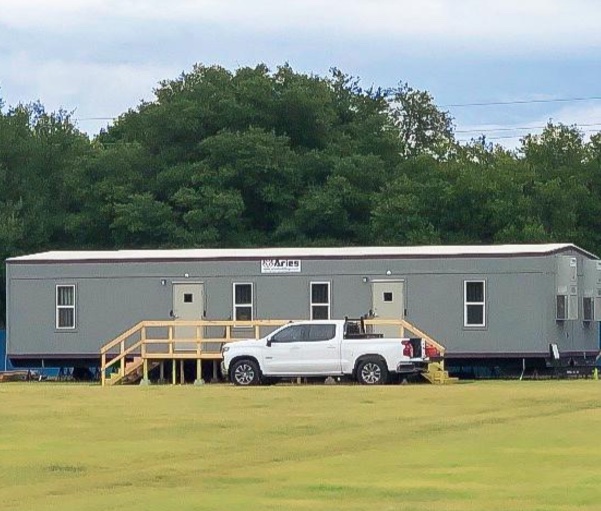 Construction Trailer with a wooden ramp and white truck parked in front, on a sunny day.