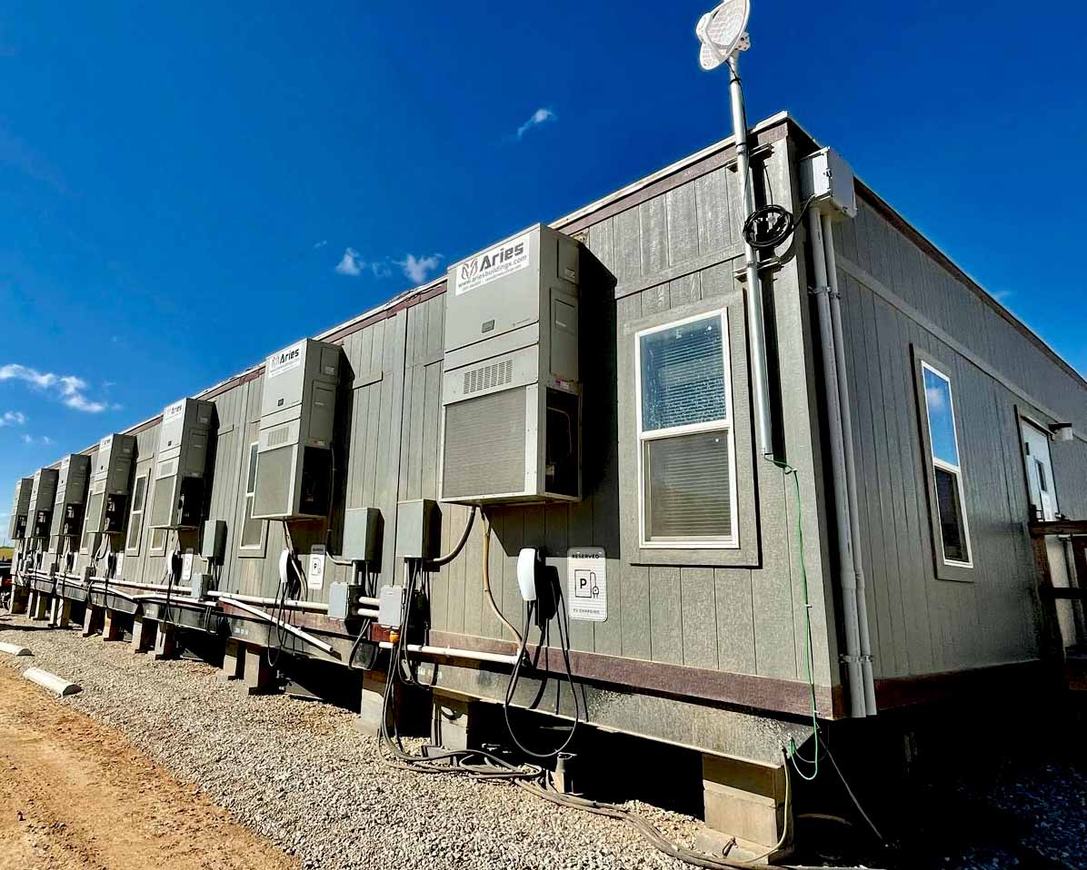 The back of a large modular office complex with HVAC systems, internet and car charging stations, on a sunny day.