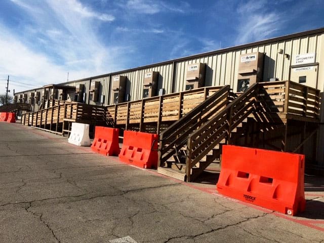 A modular building complex with wooden ramps and stairs on a sunny day, with traffic blocks alongside the building.