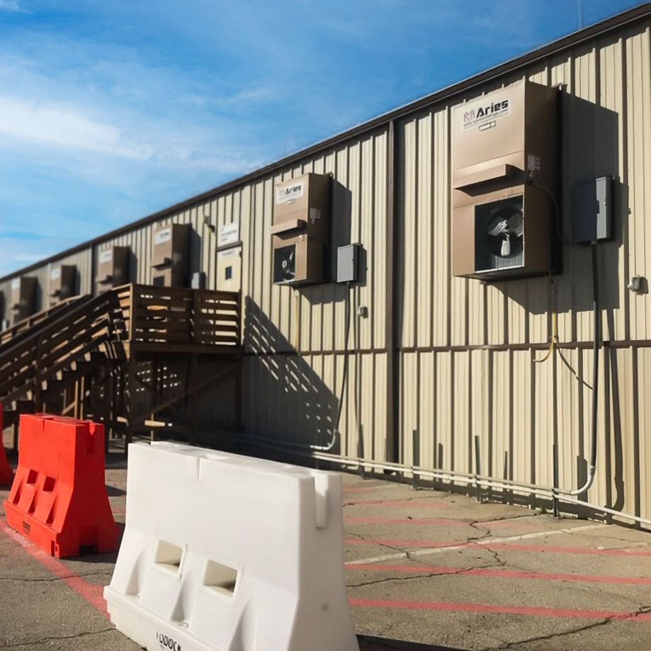 Close-up view of Aries GSA mobile office units with external HVAC systems, wooden staircases, and safety barriers set up in the lot.